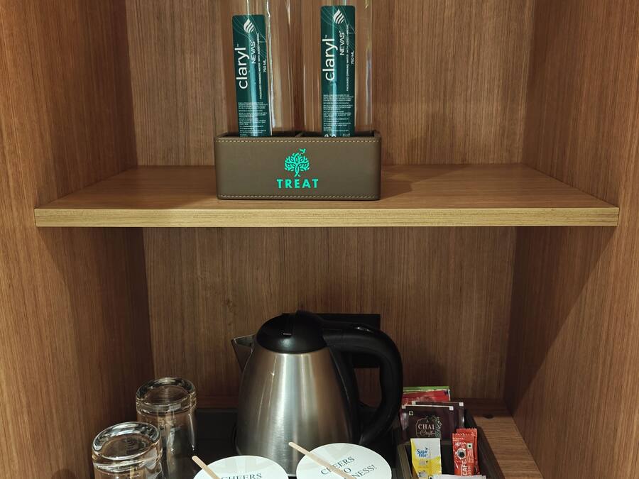 Une étagère en bois contenant des articles de toilette, notamment deux flacons de Claryl Nevis, une bouilloire, deux tasses blanches, un bocal en verre et une boîte étiquetée « Friandises ».