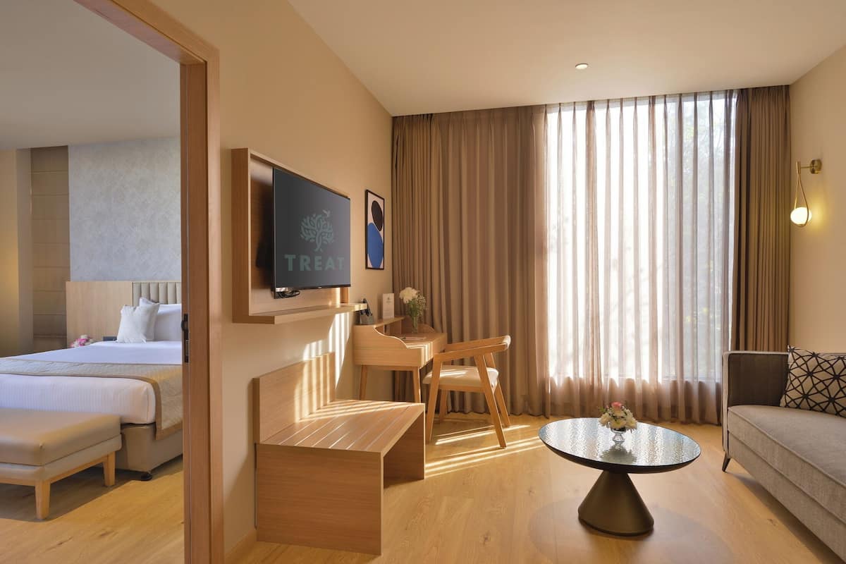 Una habitación de hotel con cama, escritorio, silla, sofá, mesa de centro y televisión.