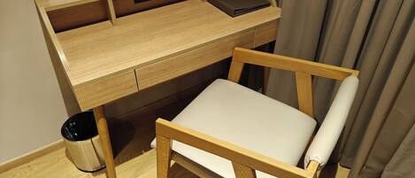 Un bureau en bois, une chaise, une poubelle et un panneau accroché au mur.