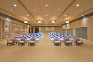 Una amplia sala de conferencias con filas de sillas y mesas, iluminación empotrada y cuadros en las paredes.