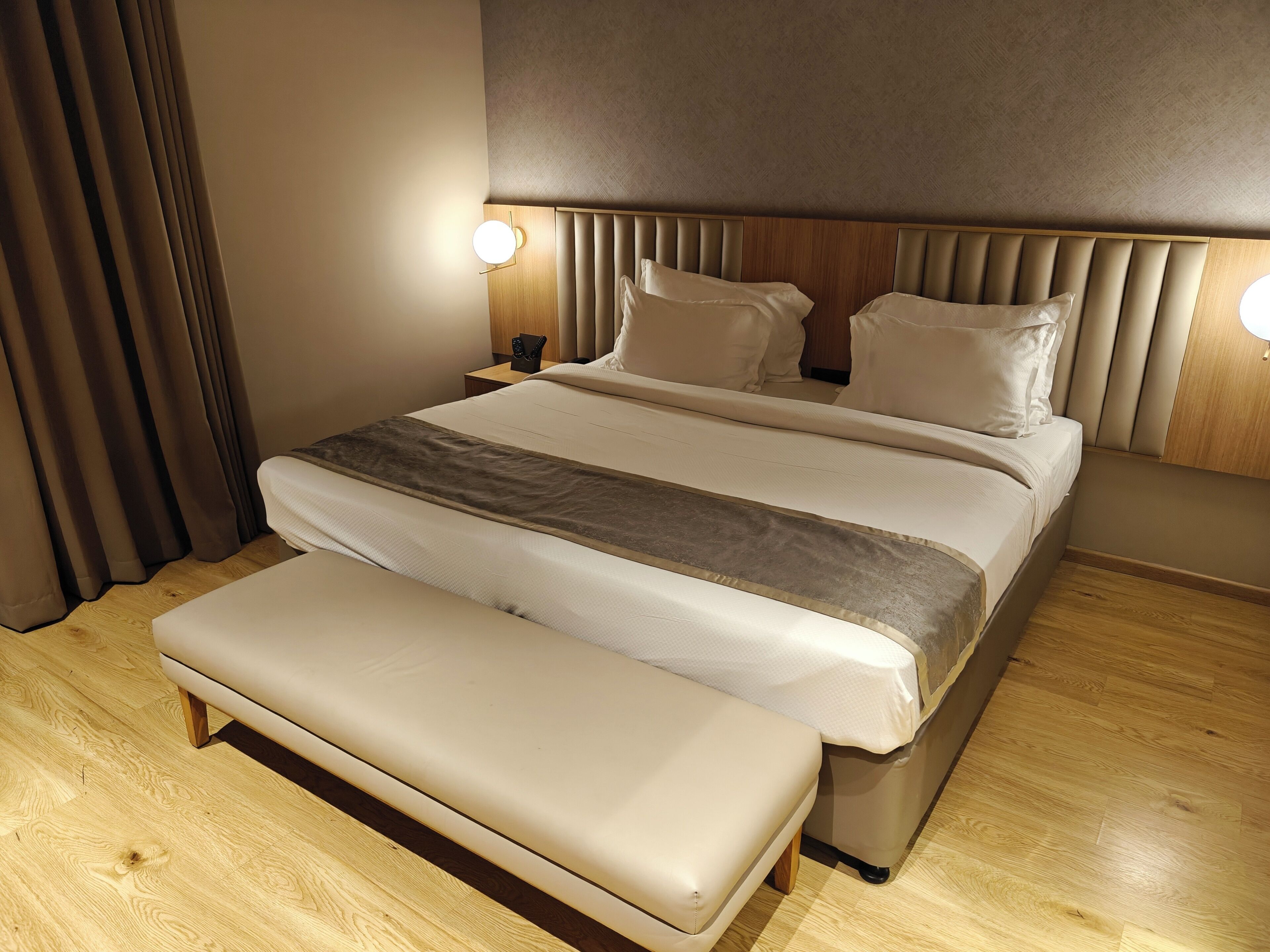 A modern hotel room with a large bed, a bench, wooden flooring, and two bedside lamps.