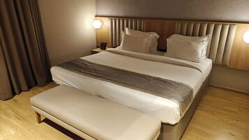 A modern hotel room with a large bed, a bench, wooden flooring, and two bedside lamps.