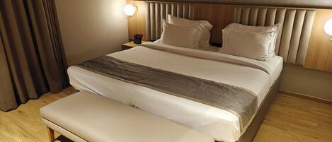 A modern hotel room with a large bed, a bench, wooden flooring, and two bedside lamps.