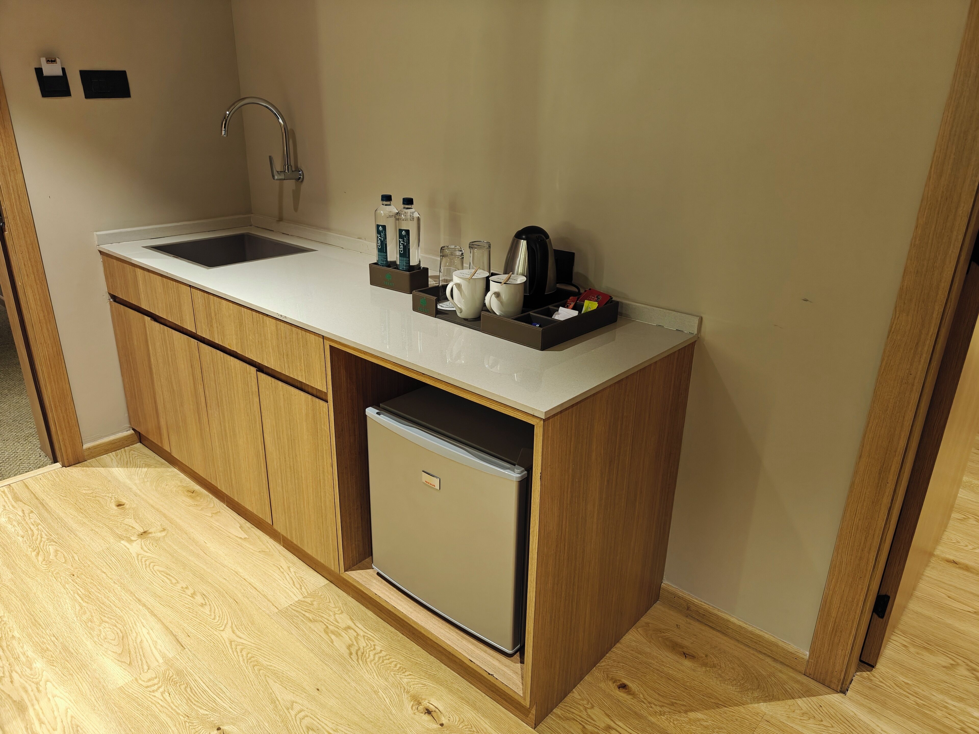 Una kitchenette compacta con un lavamanos, un refrigerador pequeño y una encimera con diversos objetos.