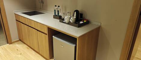 Una kitchenette compacta con un lavamanos, un refrigerador pequeño y una encimera con diversos objetos.