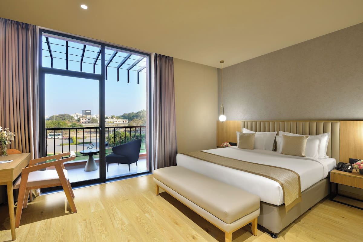 Habitación de hotel con una cama grande, un escritorio, un banco, una silla y vistas al exterior a través de una puerta corrediza de vidrio.