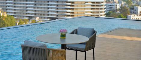 Zona de piscina en la azotea con dos sillones de mimbre y una mesa, con vistas a un paisaje urbano.