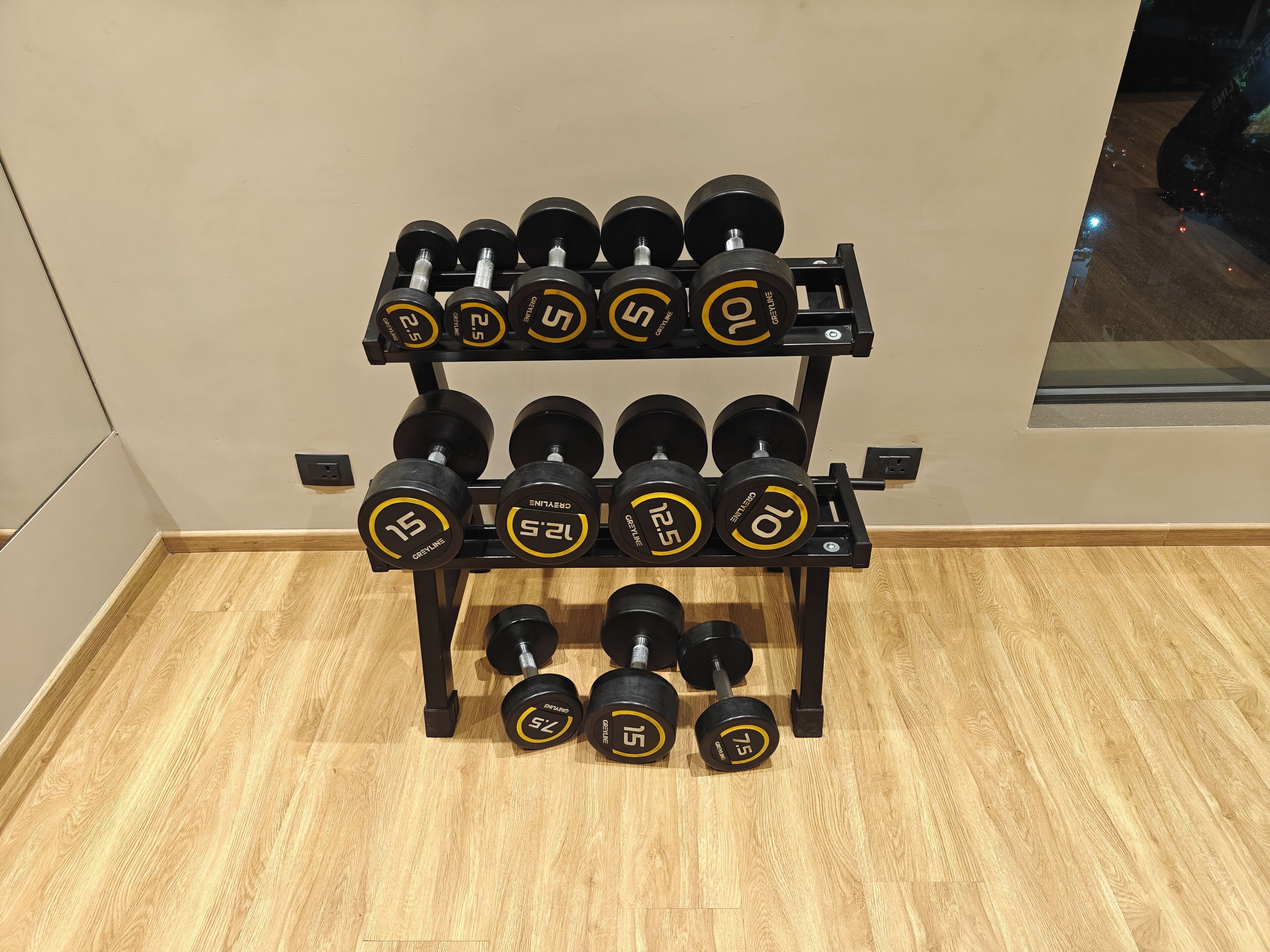 A set of adjustable dumbbells on a rack in a room with wooden flooring and a plain wall.