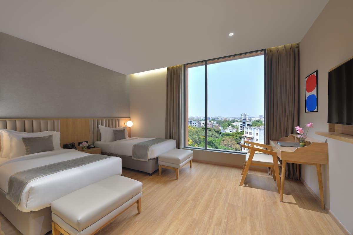 Una habitación de hotel moderna con dos camas, un escritorio y un amplio ventanal con vistas a la ciudad.