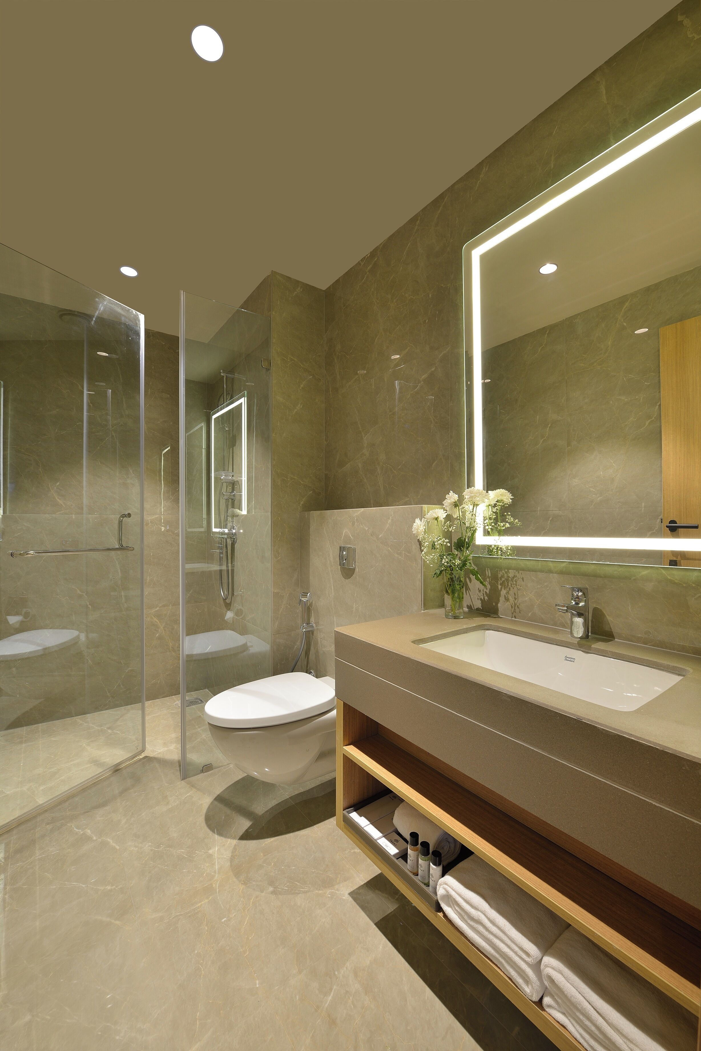 Un baño moderno con ducha envuelta en vidrio, un espejo grande y un tocador con lavabo y espacio de almacenamiento.