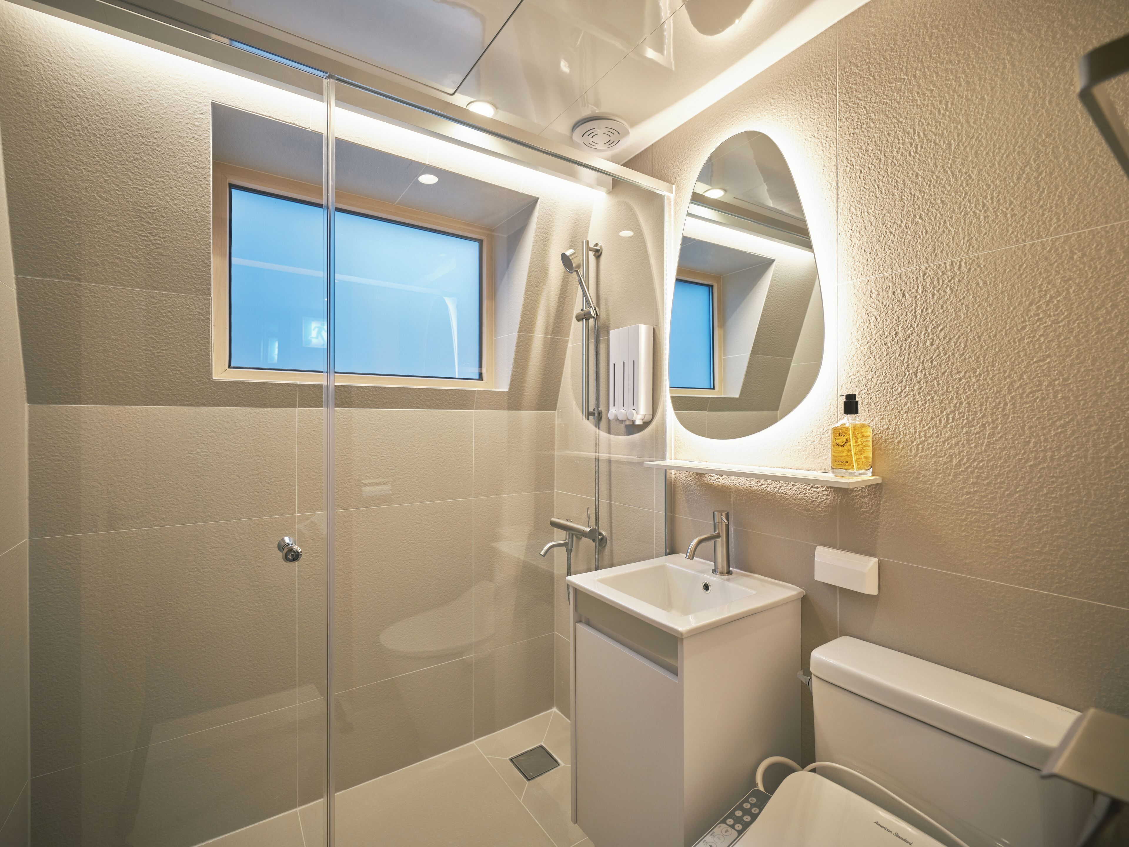 Un baño moderno con ducha envuelta en cristal, lavamanos e inodoro.