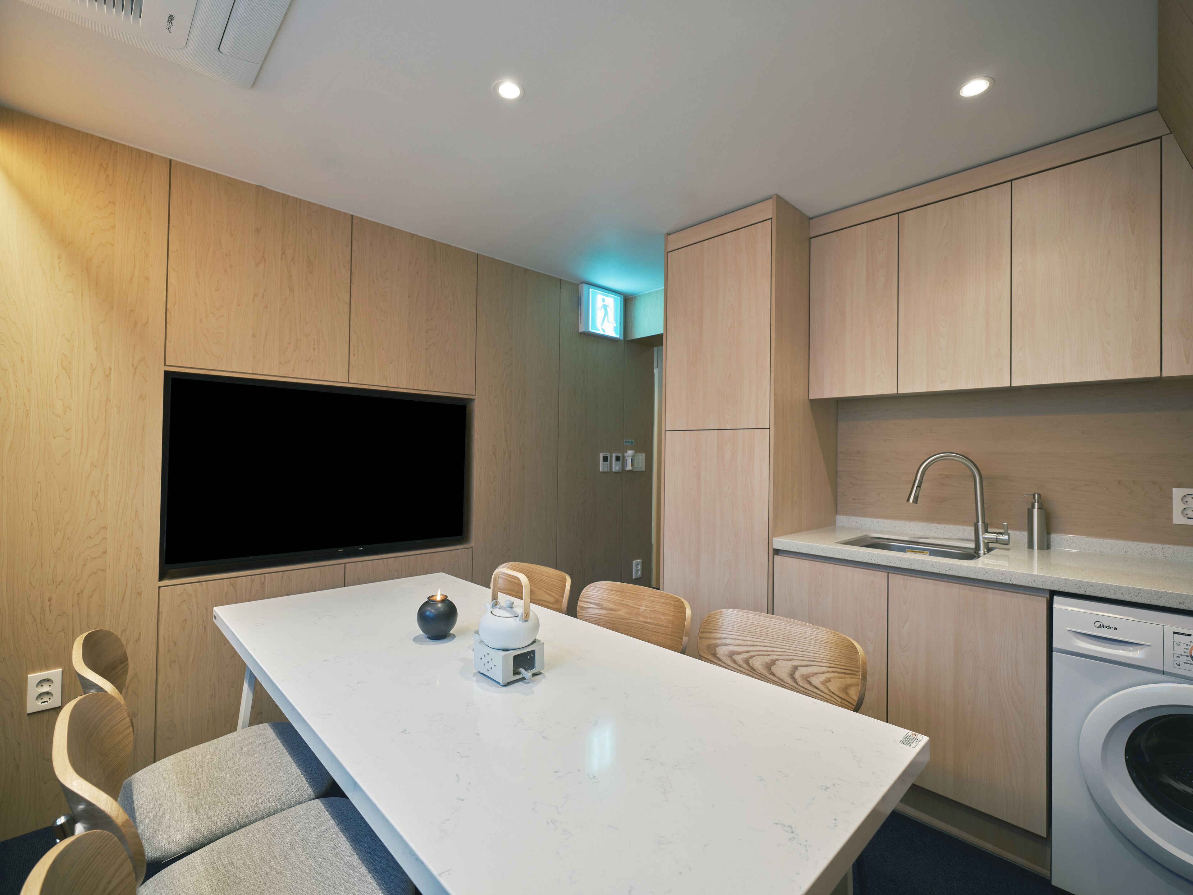 Una cocina moderna con televisor integrado, un área de comedor con mesa y sillas, y una lavadora.