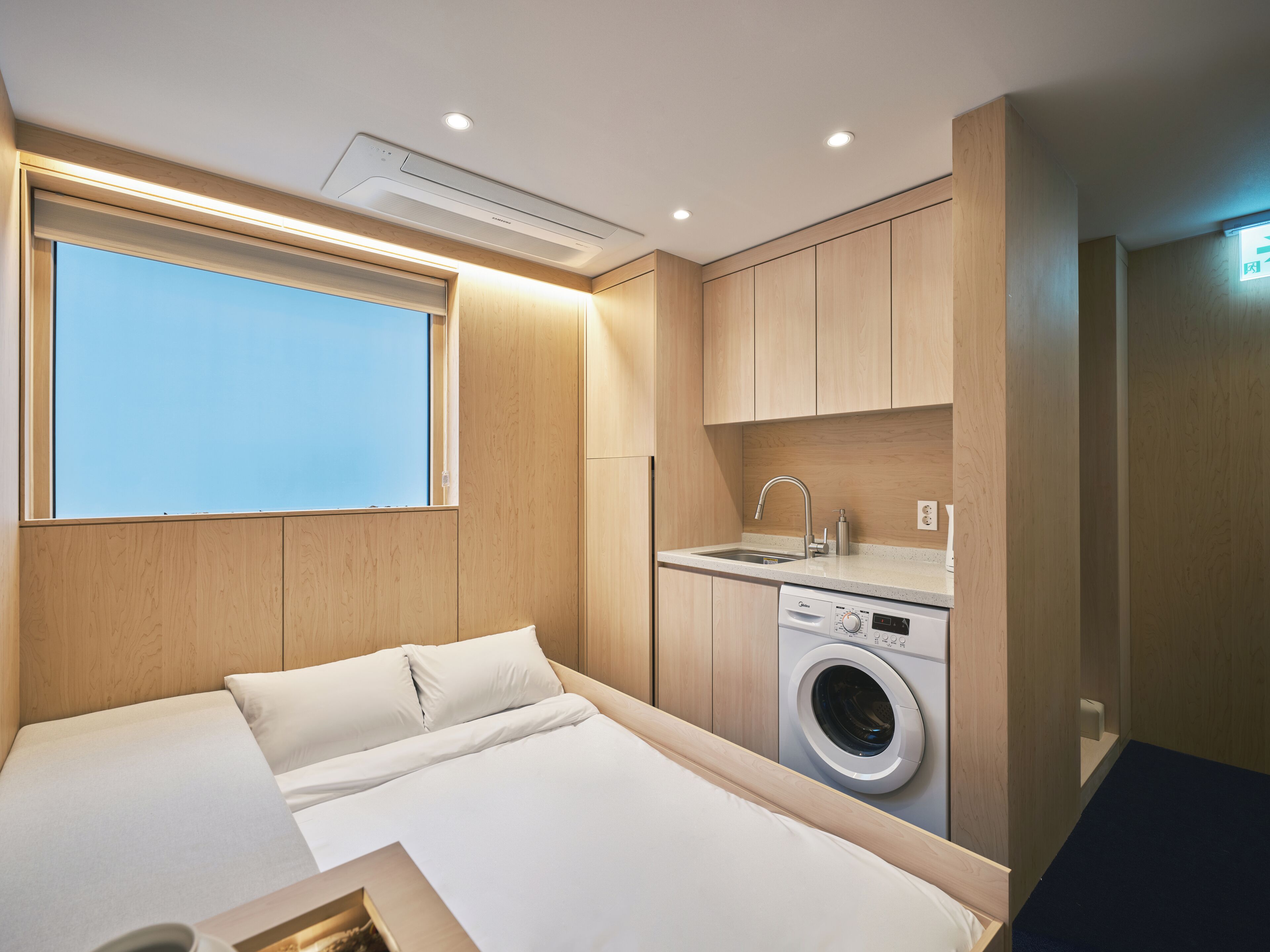 Une chambre d’hôtel de taille réduite, comprenant un lit, une machine à laver, un lavabo et une fenêtre.