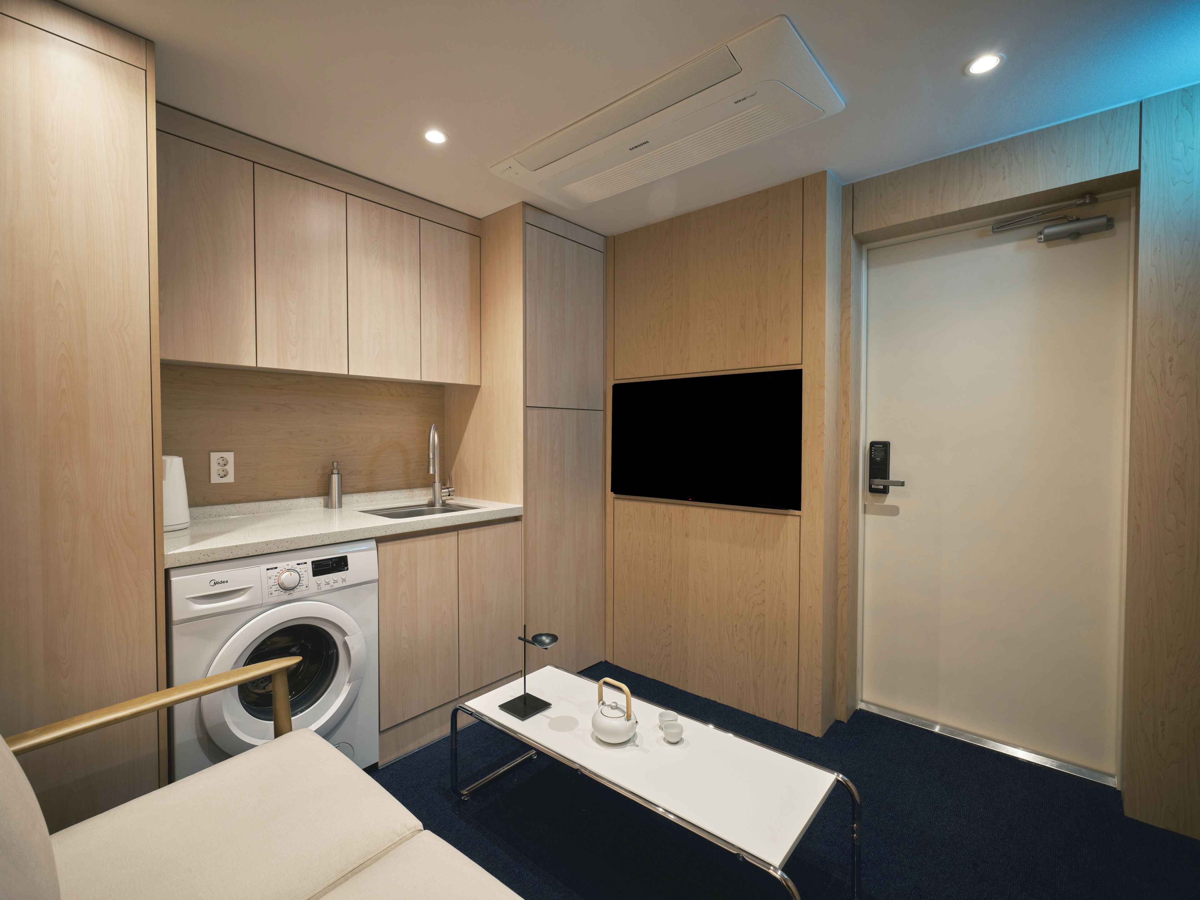 Una kitchenette compacta con lavadora, un lavabo y un televisor de pantalla plana montado en la pared.