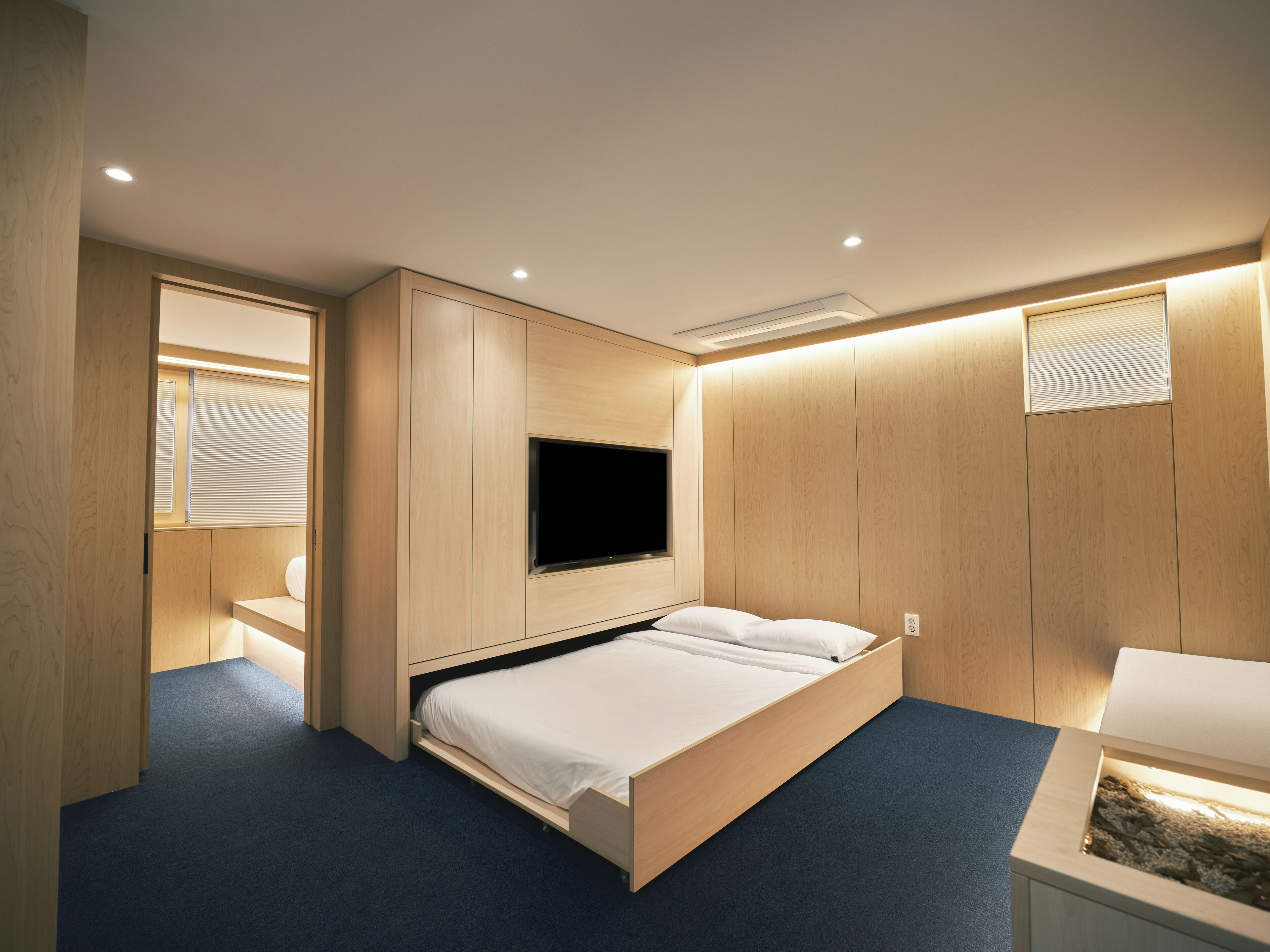 A modern bedroom with a wooden bed, built-in TV, and a small desk area.