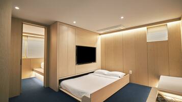 A modern bedroom with a wooden bed, built-in TV, and a small desk area.