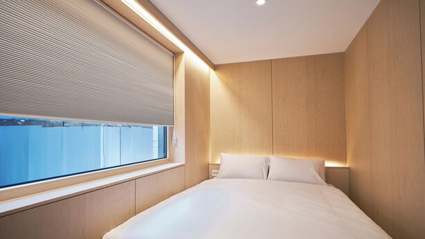 A modern bedroom with a large bed, wooden paneling, a window with blinds, and a ceiling light. - Dandelion Sinsa Branch 1 (Seoul)