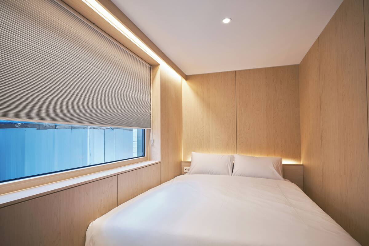 Un dormitorio moderno con una cama grande, paneles de madera, una ventana con persianas y una lámpara en el techo.