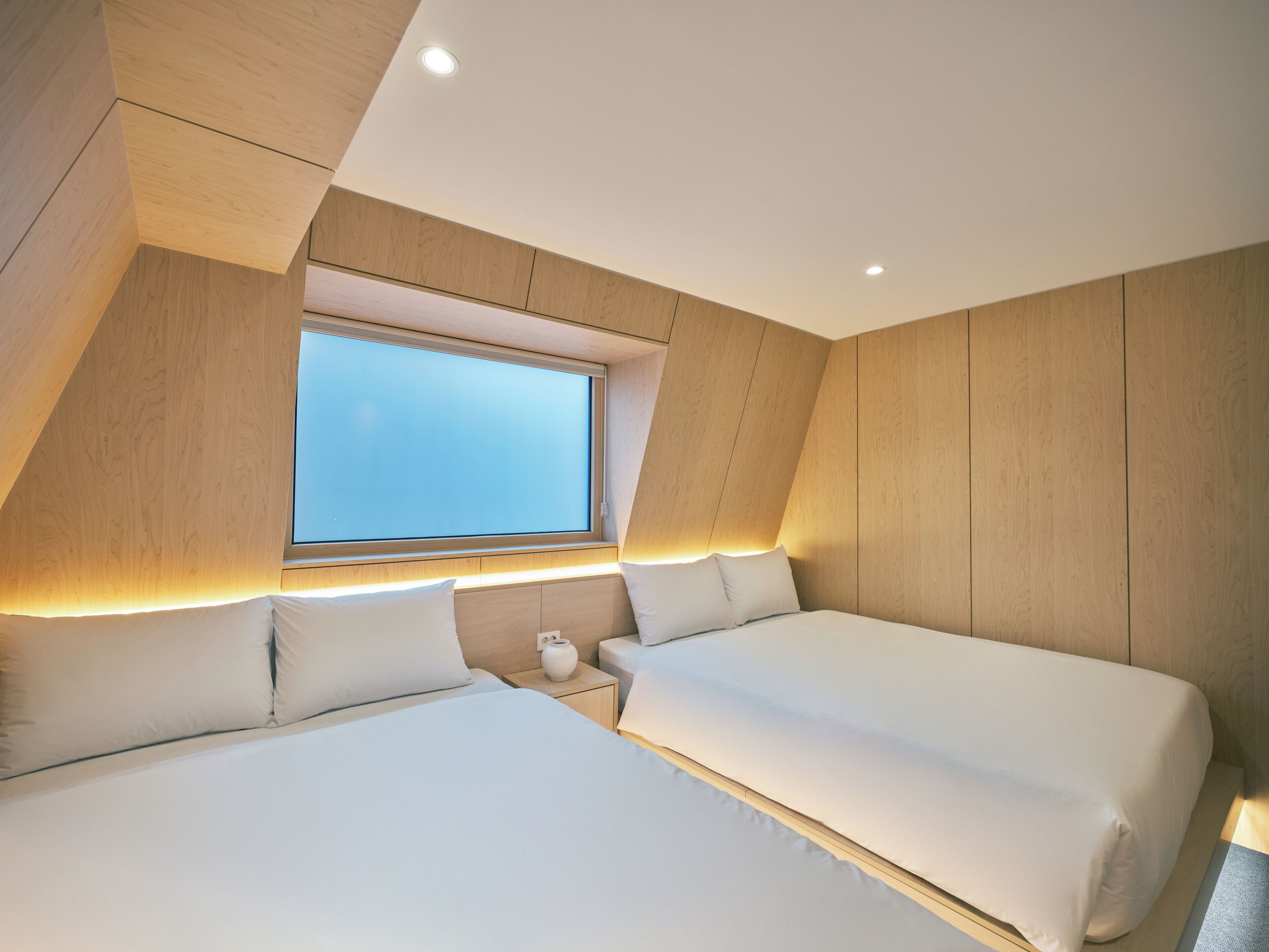 A modern bedroom with two beds, a skylight, and wooden paneling.