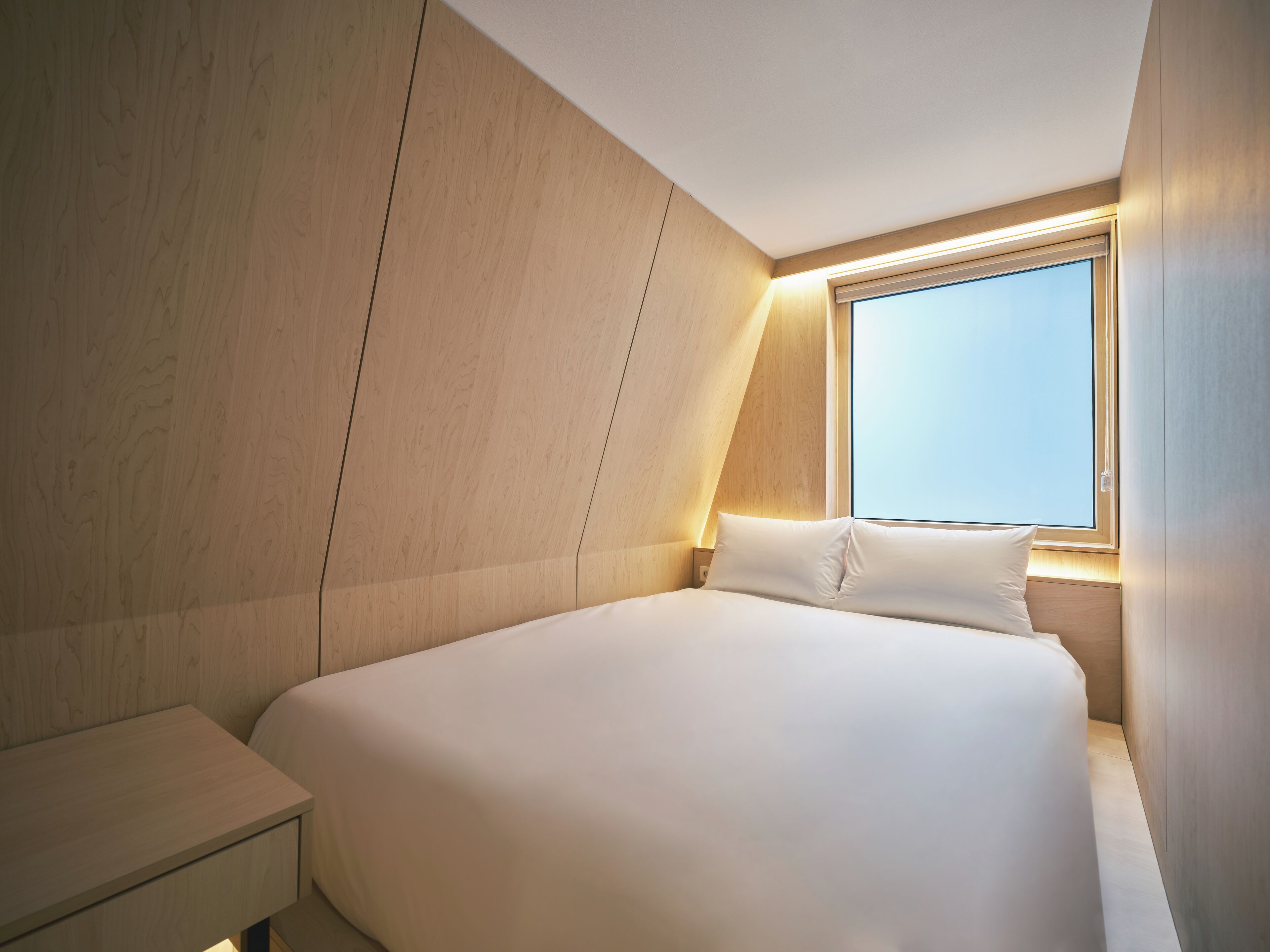 Une chambre d’hôtel moderne avec un grand lit, une table de chevet et une fenêtre donnant sur le ciel.