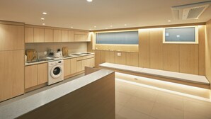 A modern kitchen with wooden cabinets, a built-in washing machine, and a large window. - Dandelion Sinsa Branch 1 (Seoul)