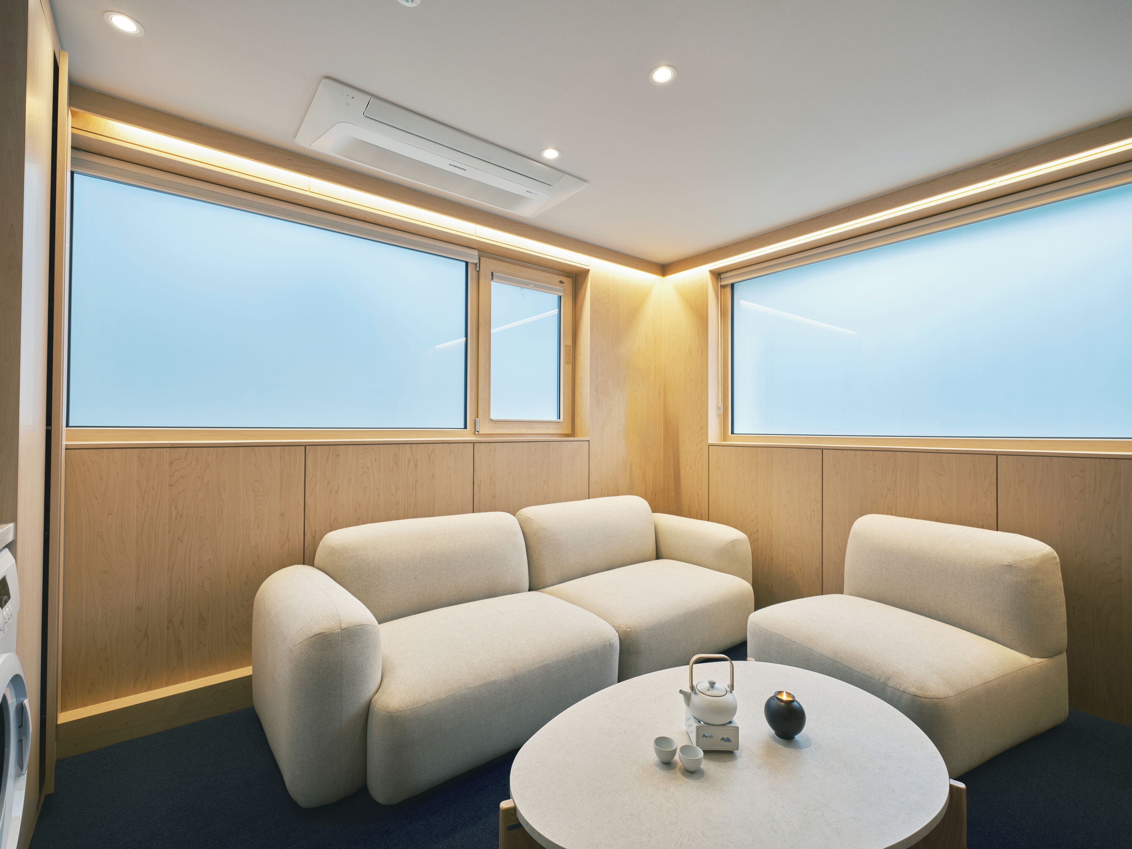 A modern room with a sofa set, a round table with a teapot and cups, and large windows with a view.