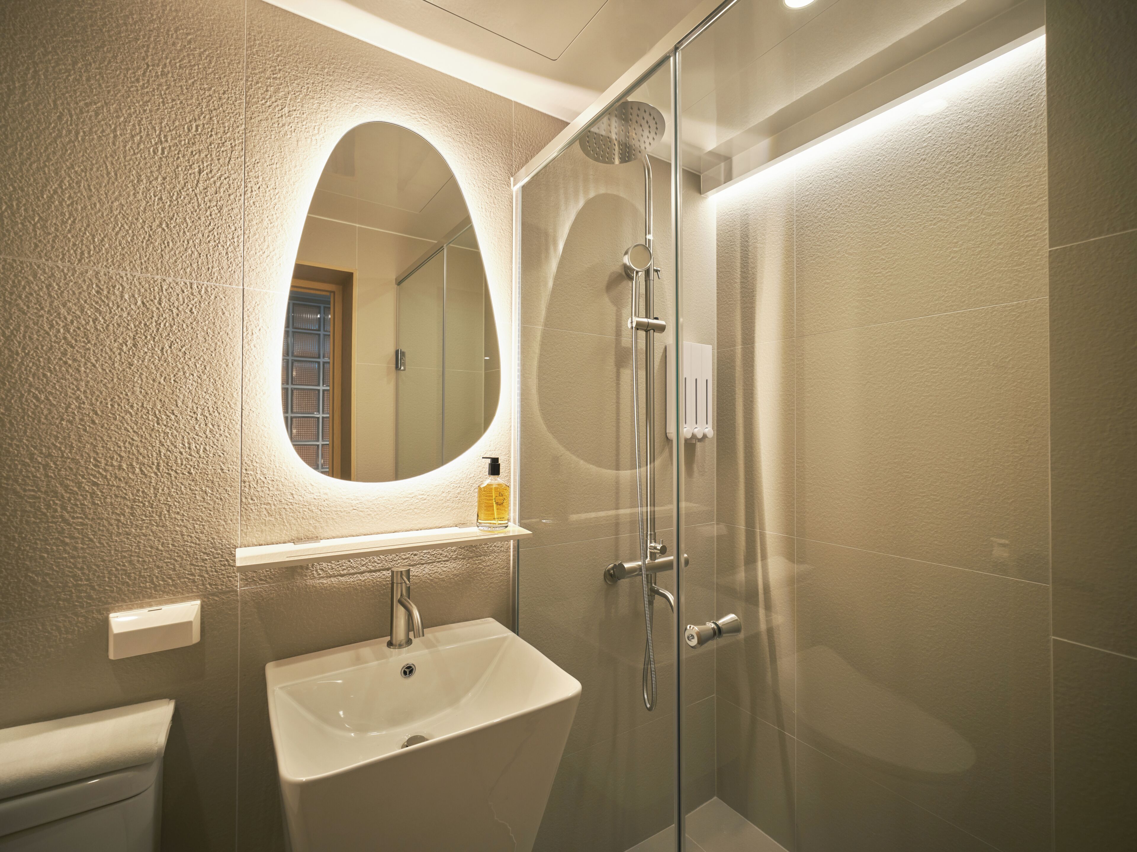 Un baño moderno con ducha de vidrio, lavamanos blanco y un espejo grande.