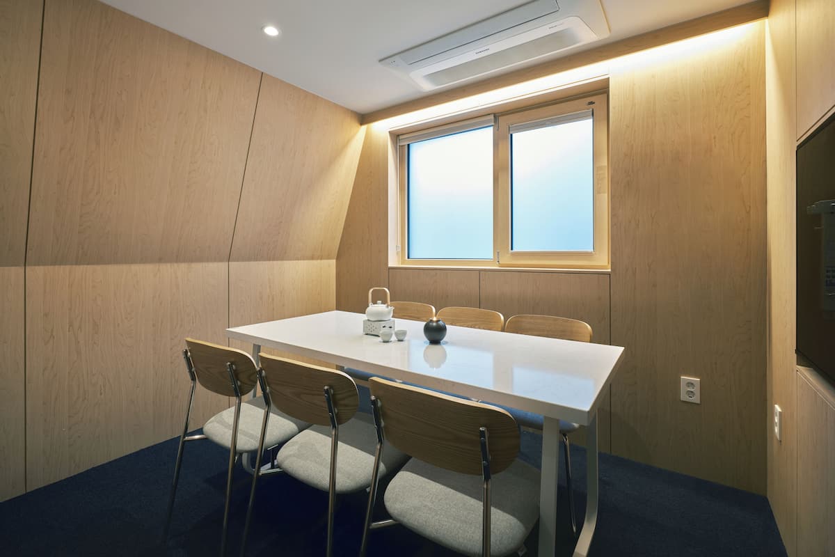 Un salón de conferencias con una mesa blanca, cuatro sillas, una ventana y un equipo de aire acondicionado.