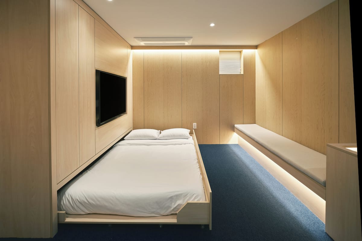 Un dormitorio moderno con cama, televisor integrado y una banca.