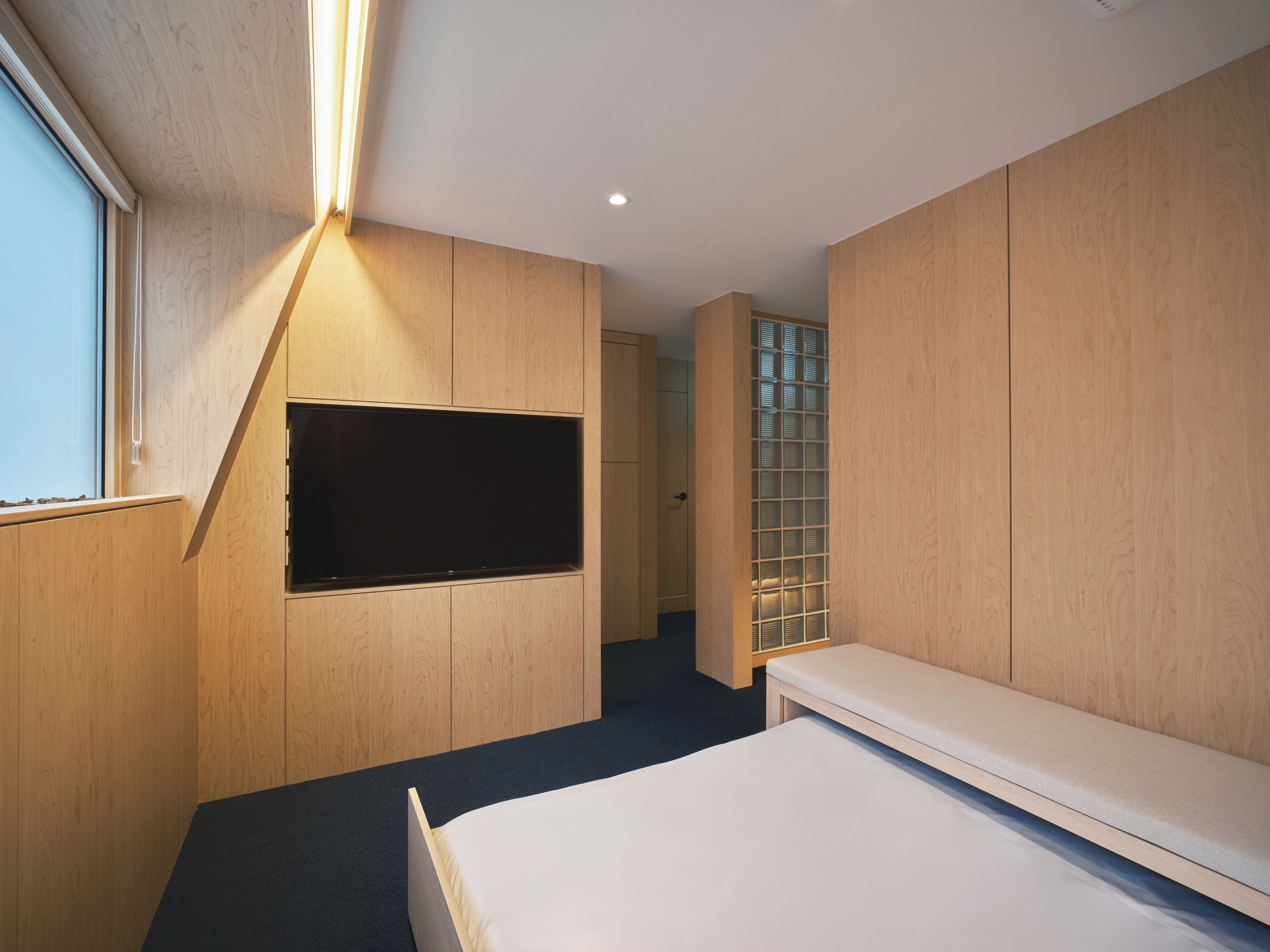 A modern bedroom with a bed, a TV mounted on the wall, and a window.