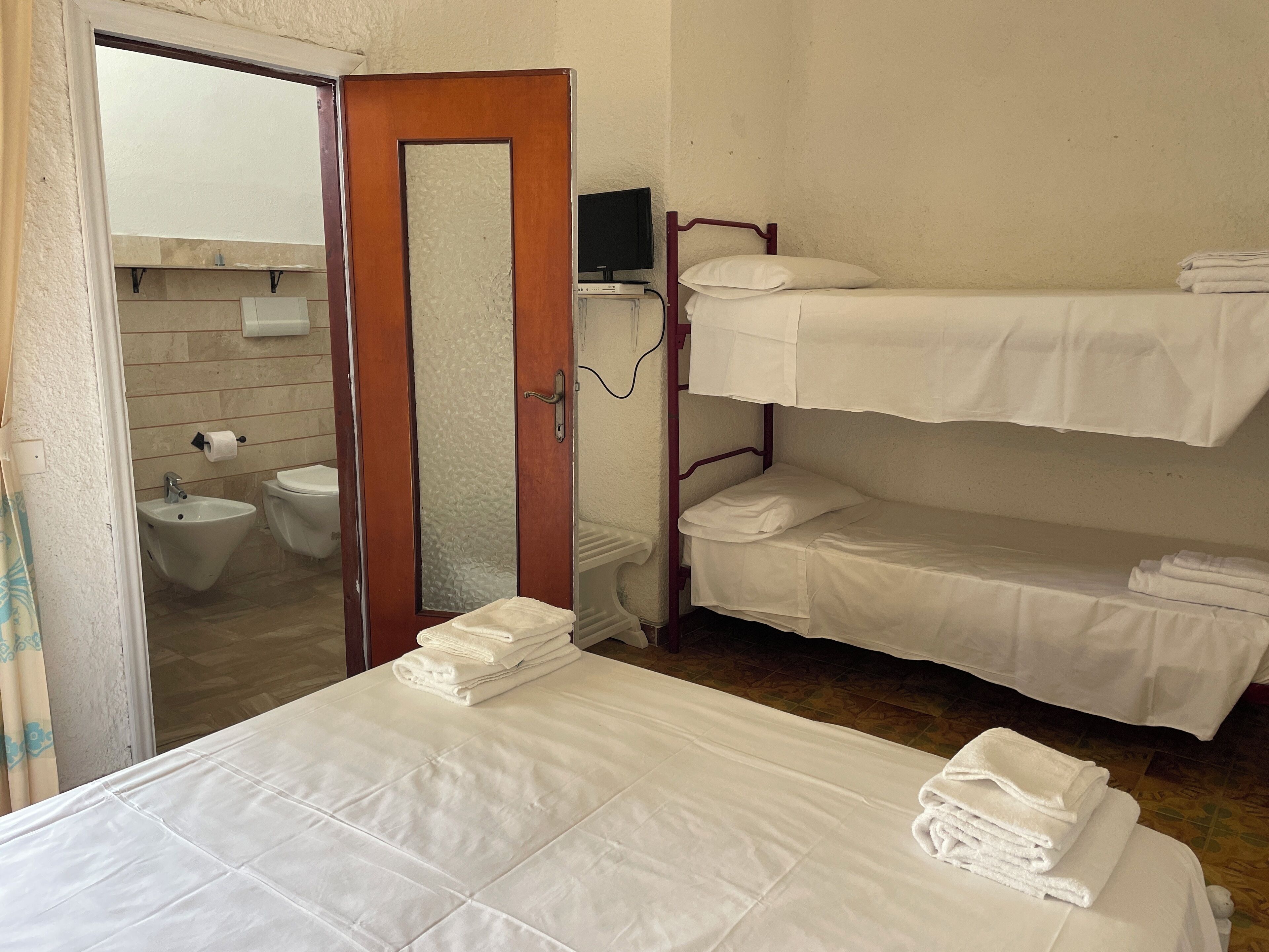 Ein Hotelzimmer mit einem Etagenbett, einem Einzelbett, einem Badezimmer inklusive Toilette, Bidet und Spiegel.
