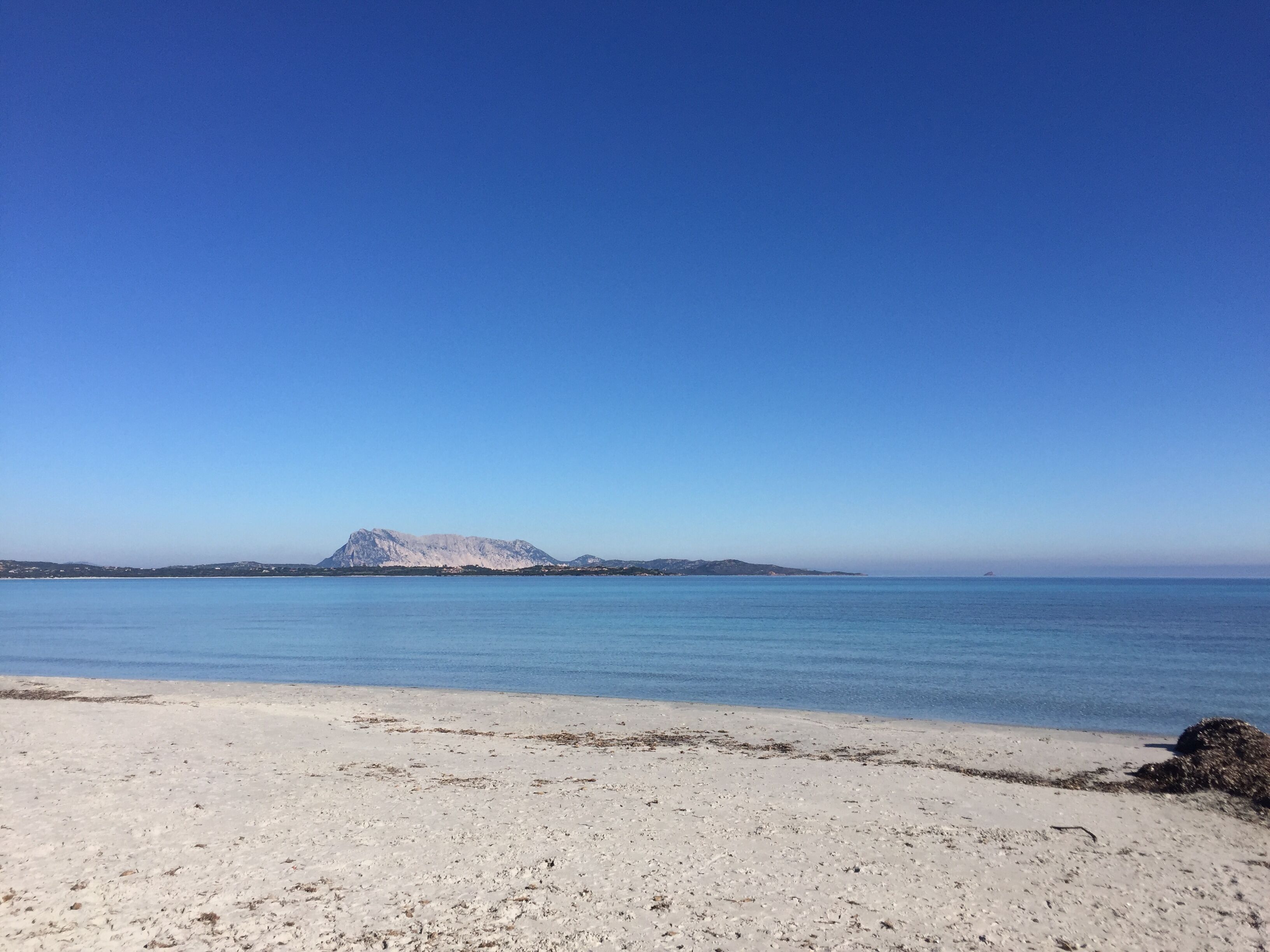A beach with a mountain in the distance and a clear blue sky.