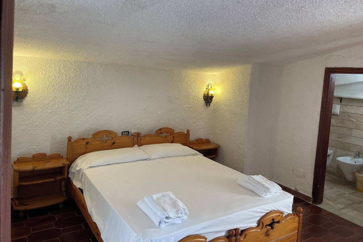 Ein Schlafzimmer mit einem Holzbett, weißen Bettwäsche, zwei Nachttischen und Wandleuchten.