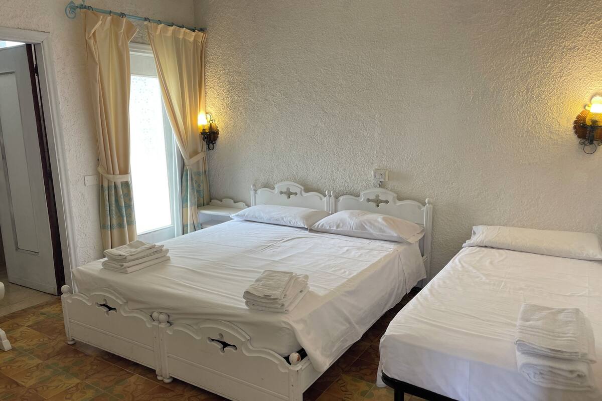 Ein Hotelzimmer mit zwei Betten, einem fensterbelaubten Fenster und Wandleuchten.