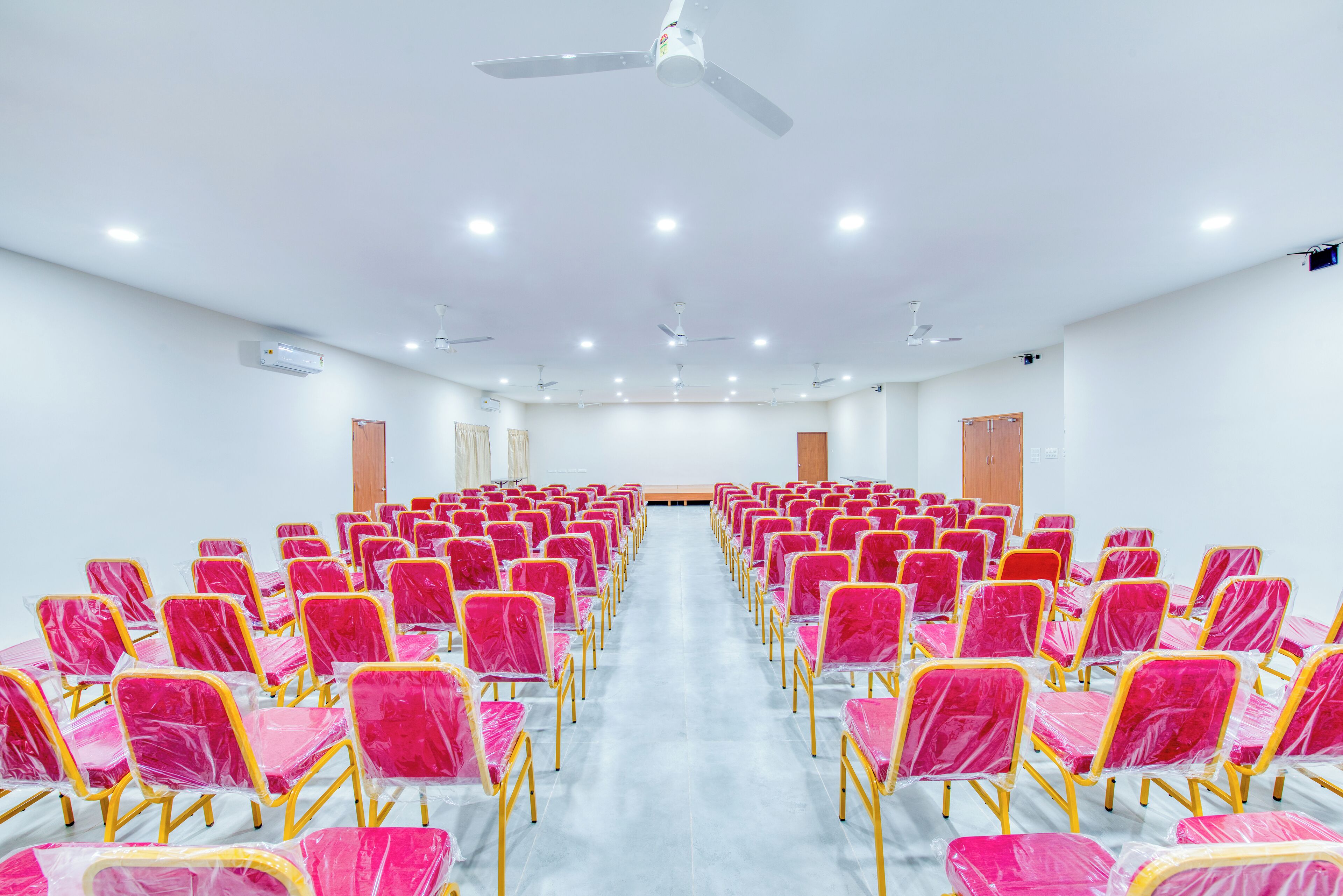 A conference room with rows of chairs, ceiling fans, and recessed lighting.
