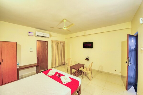 A hotel room with a bed, a desk, a chair, a TV, an air conditioner, and a wardrobe.