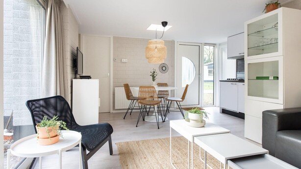 A modern living room with a dining area, a kitchen, and a large window with curtains. - Bungalow by Veluwe Sands (Kootwijk)