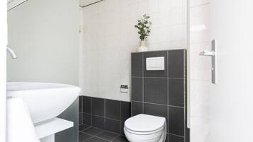 Une salle de bain moderne avec un lavabo blanc, des murs recouverts de carreaux foncés, des toilettes blanches et une plante en pot accrochée au mur.