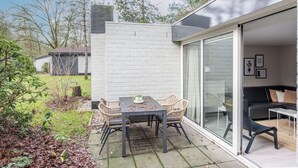 A patio with a table and chairs, a glass door leading to an interior space, and a white brick wall. - Bungalow by Veluwe Sands (Kootwijk)