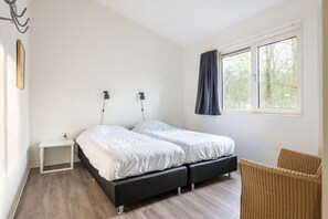 A bedroom with a bed, bedside tables, a chair, and a window with curtains. - Veluwe Forest Bungalow (Kootwijk)