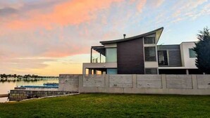 A modern house with a flat roof, large windows, and a view of a lake at sunset. - Waterfront Oasis - Panoramic Views | Infinity Pool (Kogarah Bay)