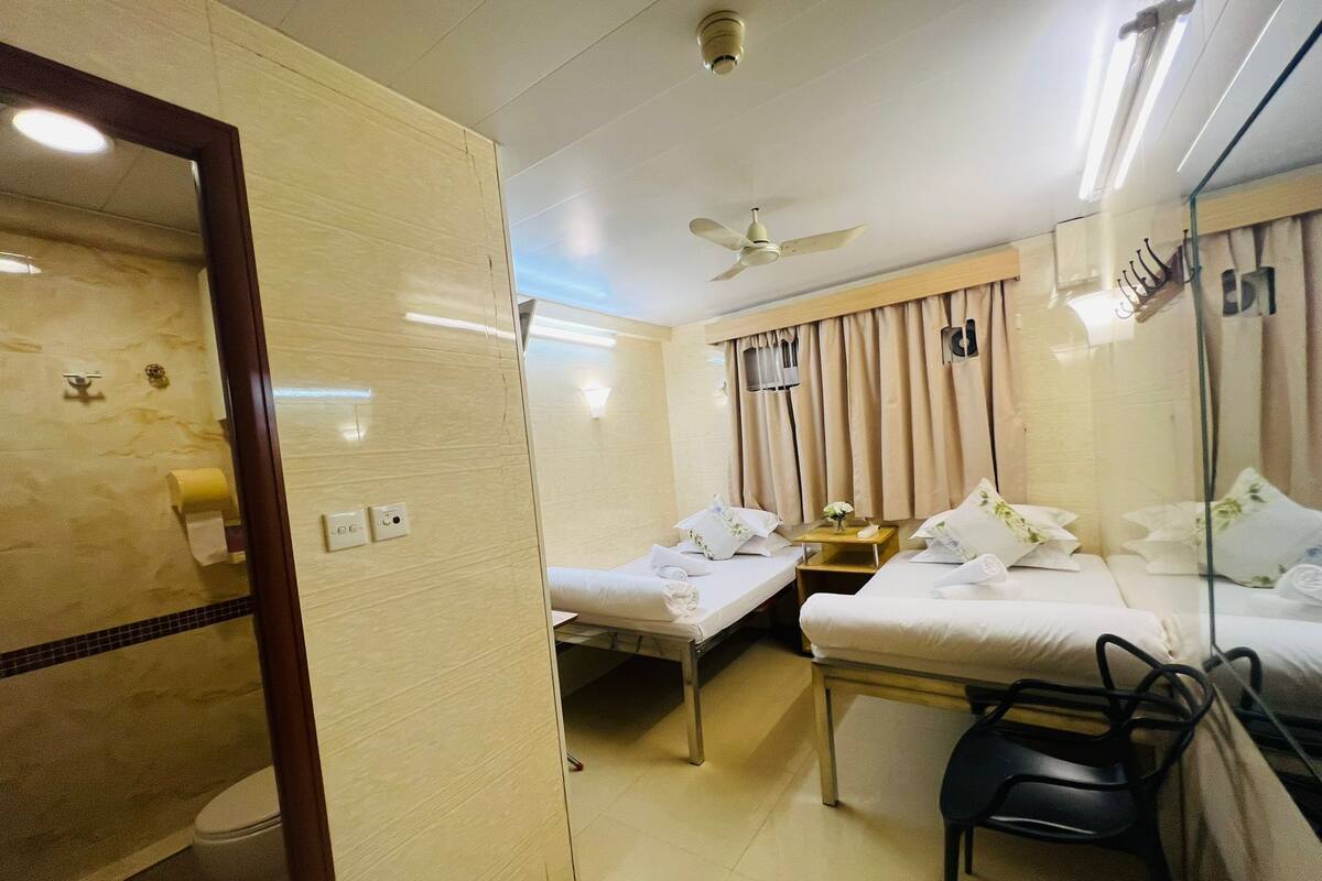 A hotel room with two single beds, a bathroom, a ceiling fan, and a mirror.