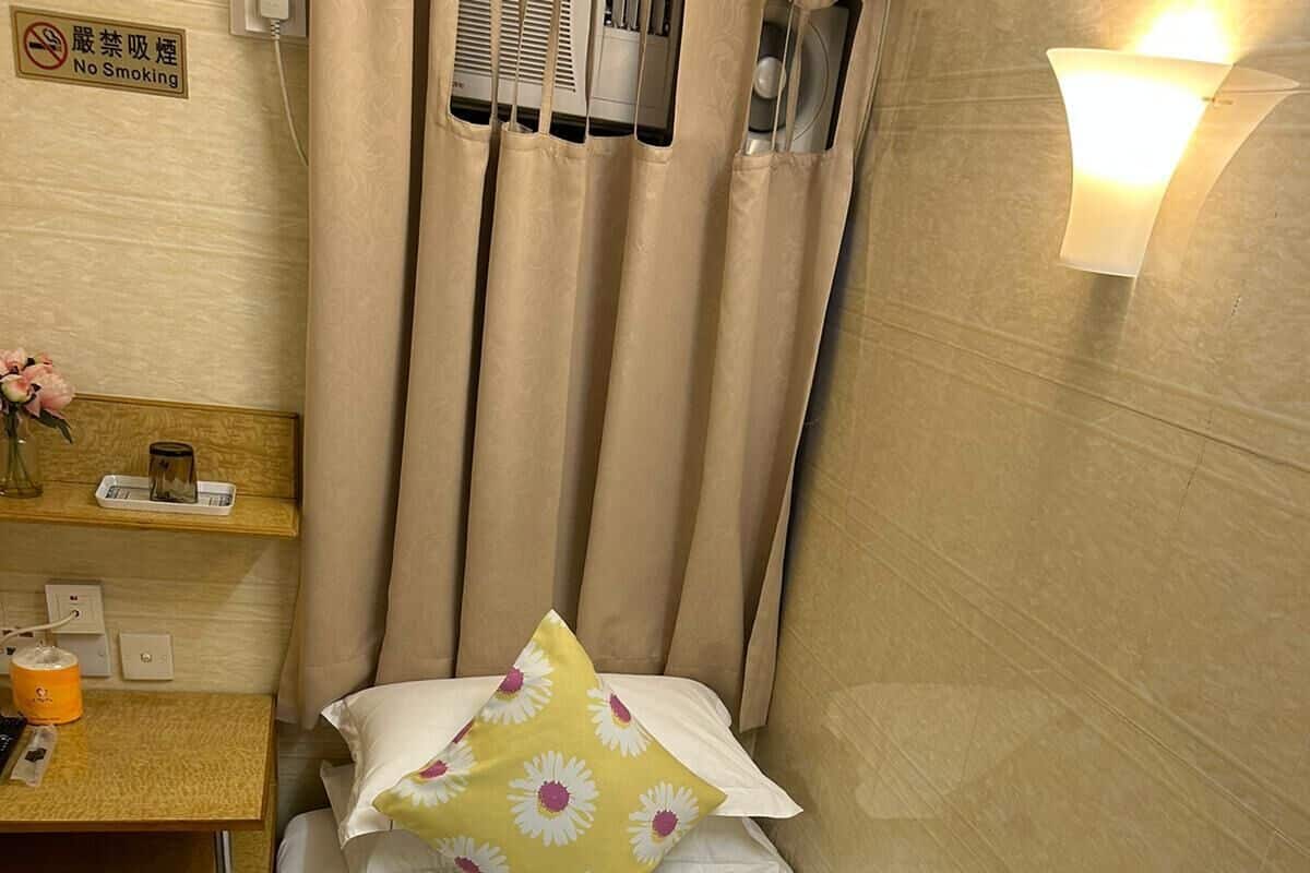 A small, neatly arranged room with a bed, a nightstand, a heater, and a wall-mounted light fixture.
