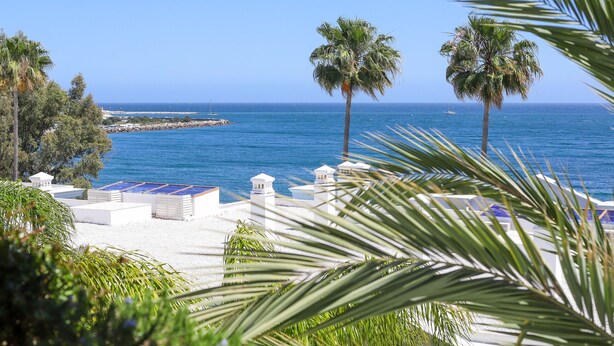 A beach view with palm trees, a clear sky, and a distant sailboat. - Doncella Beach luxury with ocean view (Estepona)