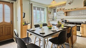 A modern kitchen with a central island, wooden cabinets, and a dining area with black chairs. - La belle étape by Interhome (Cherrueix)