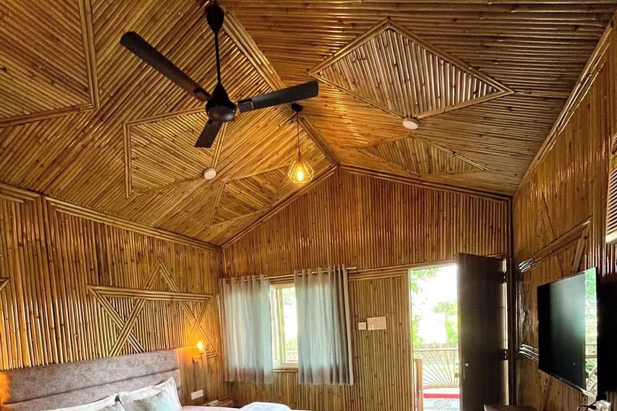 Una habitación con una cama, ventilador de techo, televisor y paredes de madera.