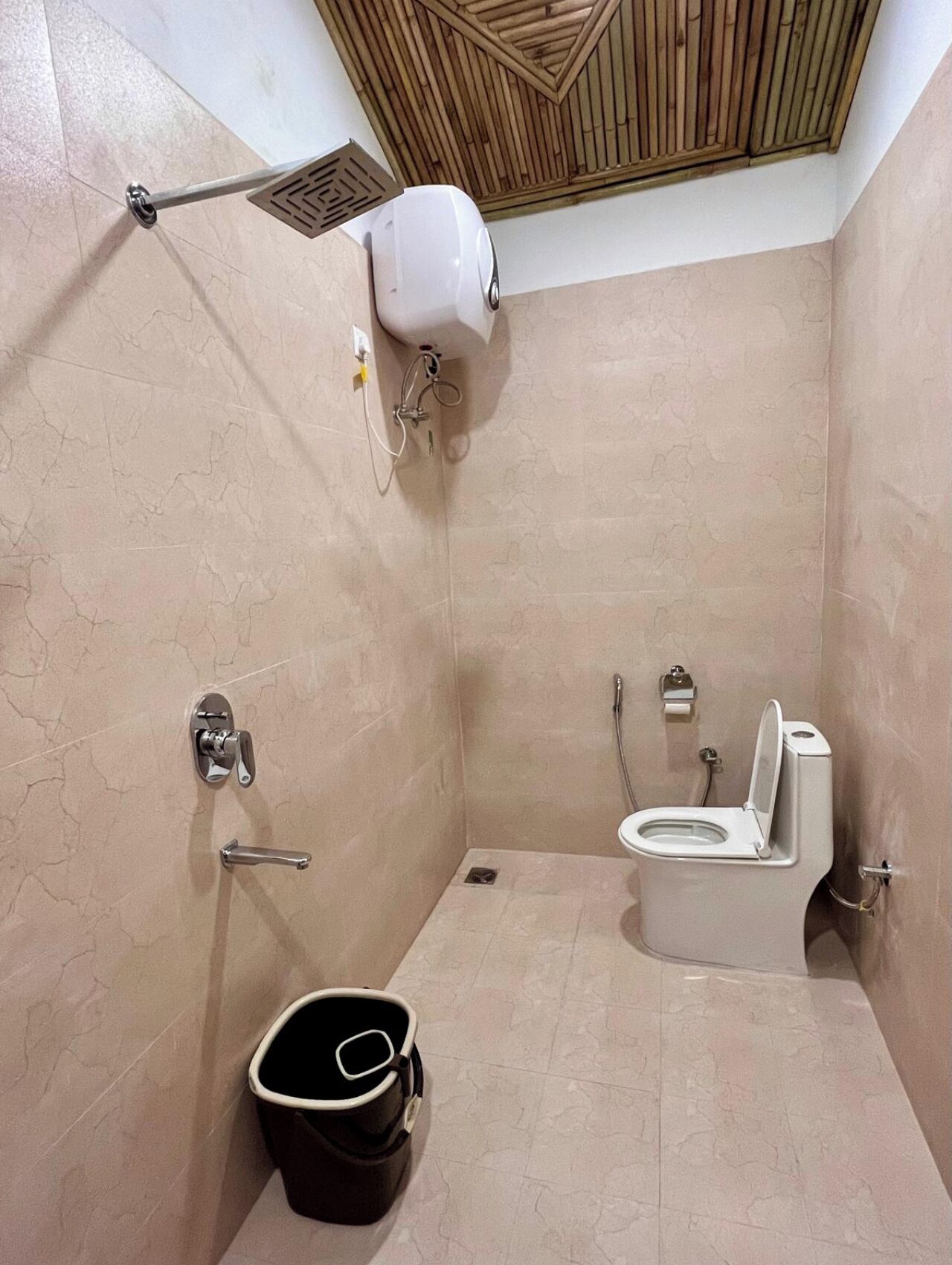Un baño pequeño con azulejos, ducha, inodoro y un balde.