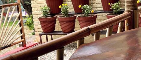 A wooden table and chairs in an outdoor seating area with potted plants and a brick wall in the background.