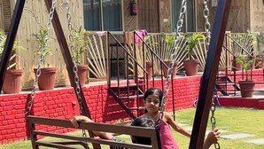 A swing set in a garden with a brick wall and potted plants.
