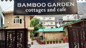 Experience a welcoming atmosphere at Bamboo Garden, where cottages and a cafe await, surrounded by a beautifully maintained garden with a paved walkway and potted plants.